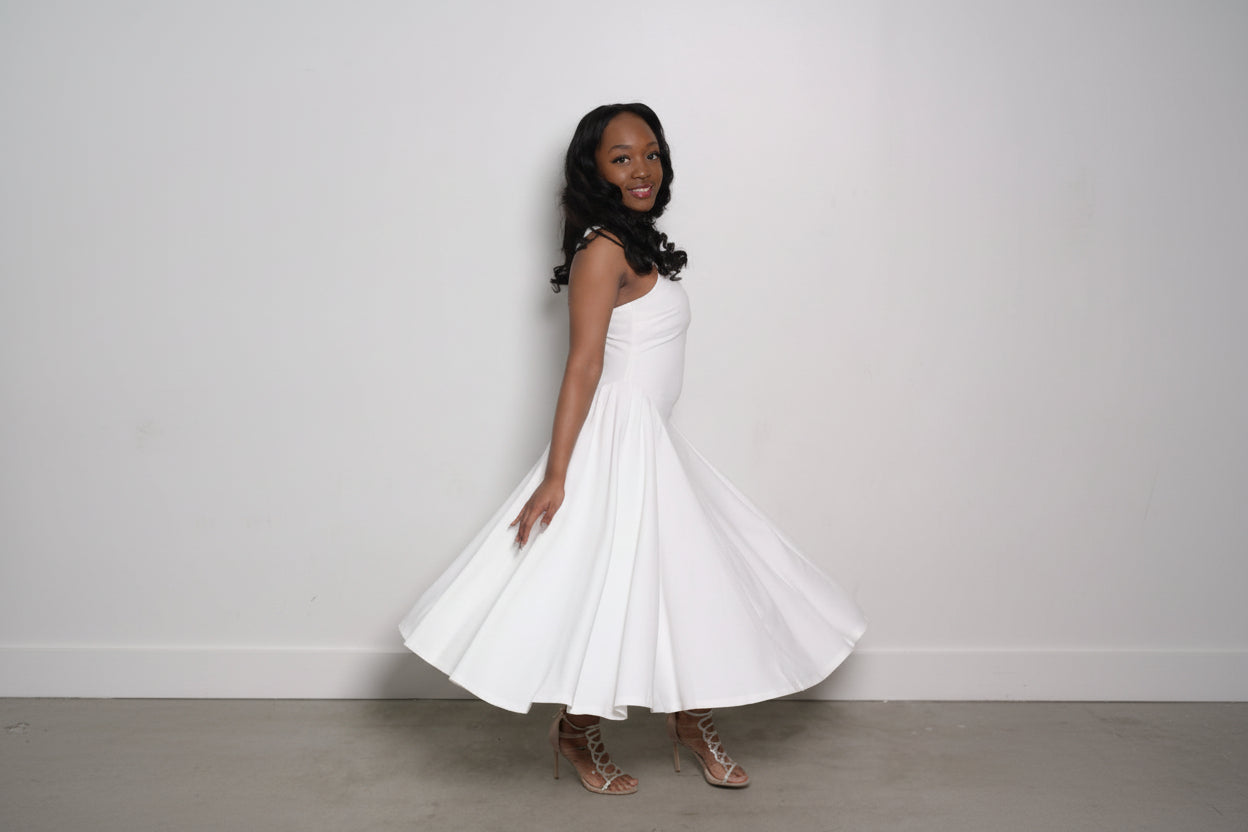 Woman in a white dress standing against a plain background